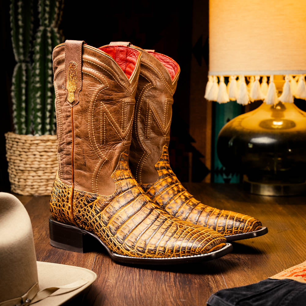 The Marco Di Milano Tucson Mustard Brown men's Western boots feature brown leather uppers and yellow genuine caiman belly skin lowers; one boot stands upright, the other shows the signature square toe cowboy boot sole.