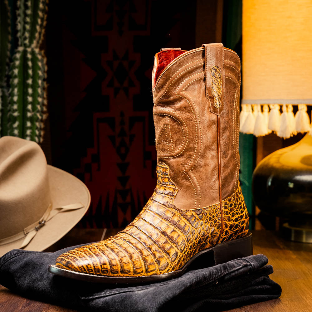 The Marco Di Milano Tucson Mustard Brown men's Western boots feature brown leather uppers and yellow genuine caiman belly skin lowers; one boot stands upright, the other shows the signature square toe cowboy boot sole.