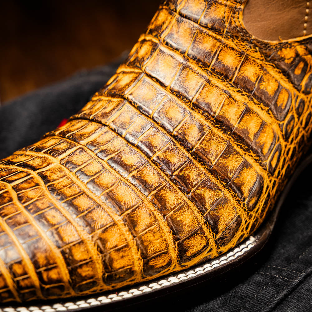 The Marco Di Milano Tucson Mustard Brown men's Western boots feature brown leather uppers and yellow genuine caiman belly skin lowers; one boot stands upright, the other shows the signature square toe cowboy boot sole.