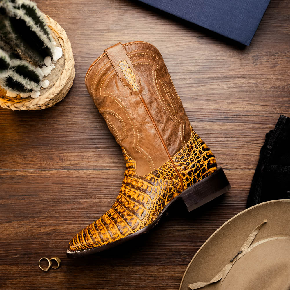 The Marco Di Milano Tucson Mustard Brown men's Western boots feature brown leather uppers and yellow genuine caiman belly skin lowers; one boot stands upright, the other shows the signature square toe cowboy boot sole.