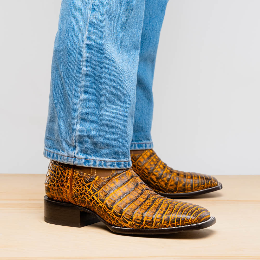 The Marco Di Milano Tucson Mustard Brown men's Western boots feature brown leather uppers and yellow genuine caiman belly skin lowers; one boot stands upright, the other shows the signature square toe cowboy boot sole.