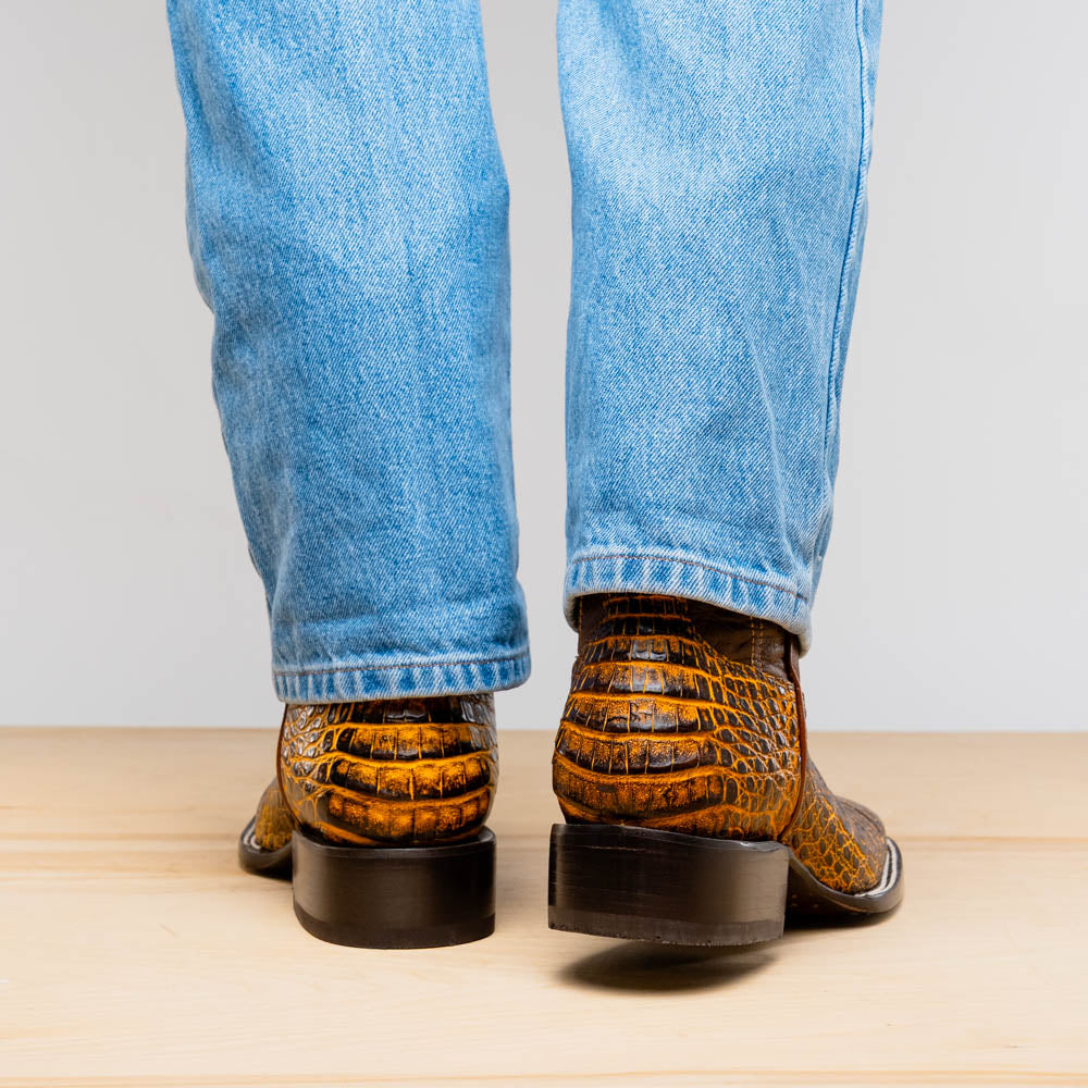 The Marco Di Milano Tucson Mustard Brown men's Western boots feature brown leather uppers and yellow genuine caiman belly skin lowers; one boot stands upright, the other shows the signature square toe cowboy boot sole.