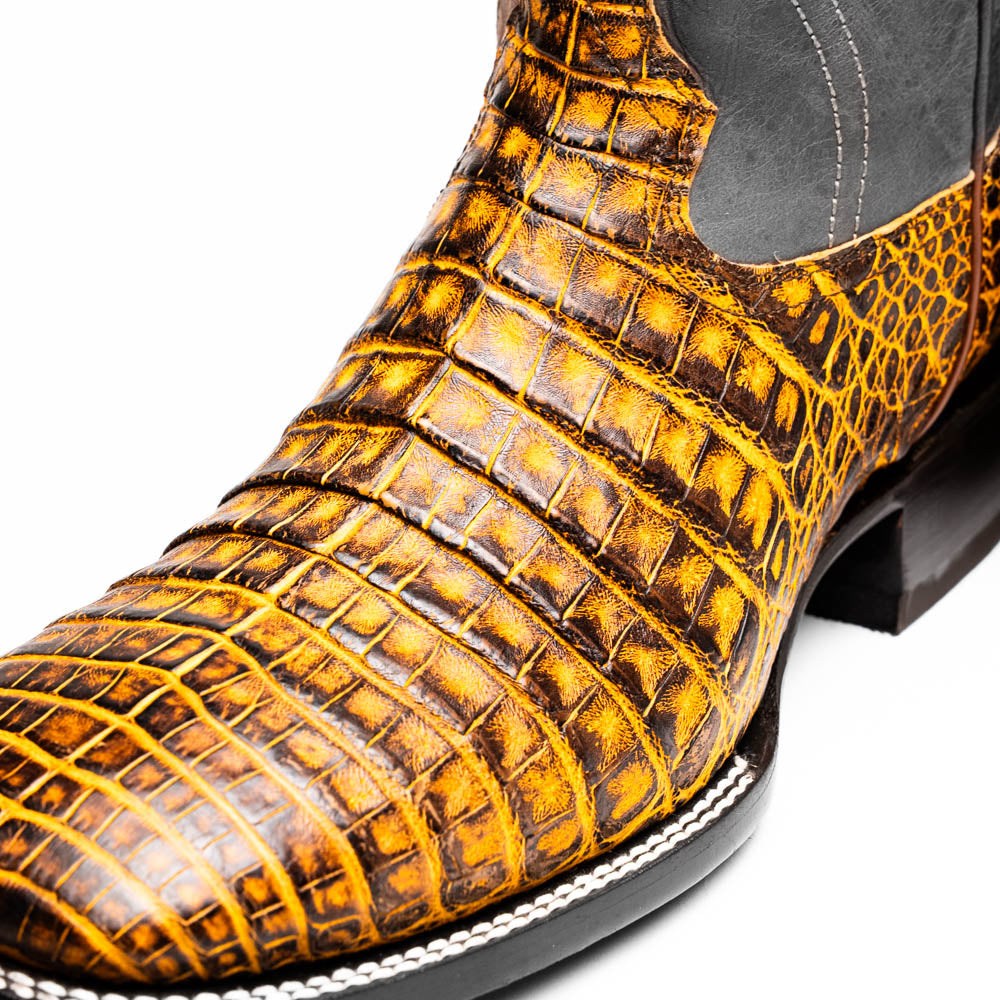 The Marco Di Milano Tucson Mustard Brown men's Western boots feature brown leather uppers and yellow genuine caiman belly skin lowers; one boot stands upright, the other shows the signature square toe cowboy boot sole.