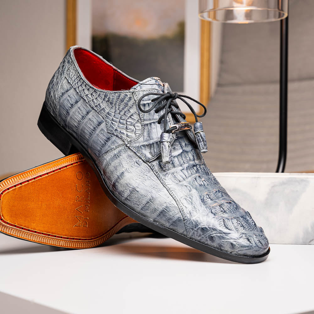 The Tulum Gray by Marco Di Milano is a luxury men’s dress shoe in genuine caiman crocodile leather, featuring black laces and a metal ornament, shown with one shoe on its side to display the branded leather sole.