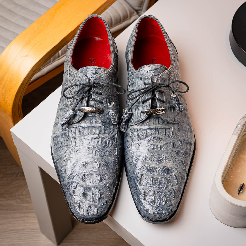 The Tulum Gray by Marco Di Milano is a luxury men’s dress shoe in genuine caiman crocodile leather, featuring black laces and a metal ornament, shown with one shoe on its side to display the branded leather sole.