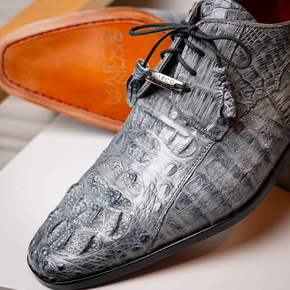 The Tulum Gray by Marco Di Milano is a luxury men’s dress shoe in genuine caiman crocodile leather, featuring black laces and a metal ornament, shown with one shoe on its side to display the branded leather sole.