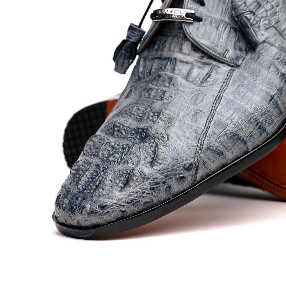 The Tulum Gray by Marco Di Milano is a luxury men’s dress shoe in genuine caiman crocodile leather, featuring black laces and a metal ornament, shown with one shoe on its side to display the branded leather sole.