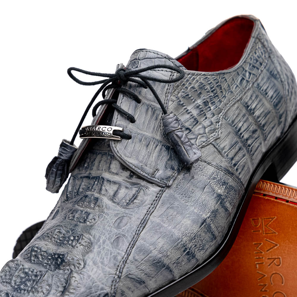 The Tulum Gray by Marco Di Milano is a luxury men’s dress shoe in genuine caiman crocodile leather, featuring black laces and a metal ornament, shown with one shoe on its side to display the branded leather sole.