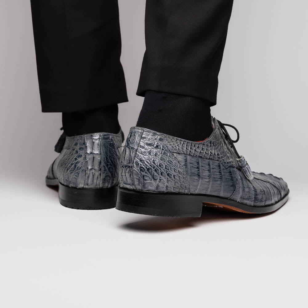 The Tulum Gray by Marco Di Milano is a luxury men’s dress shoe in genuine caiman crocodile leather, featuring black laces and a metal ornament, shown with one shoe on its side to display the branded leather sole.