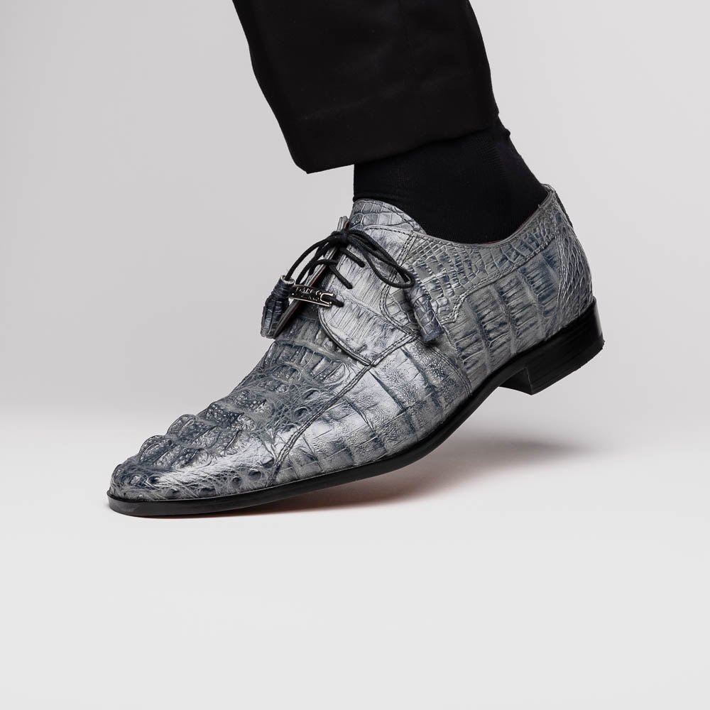 The Tulum Gray by Marco Di Milano is a luxury men’s dress shoe in genuine caiman crocodile leather, featuring black laces and a metal ornament, shown with one shoe on its side to display the branded leather sole.