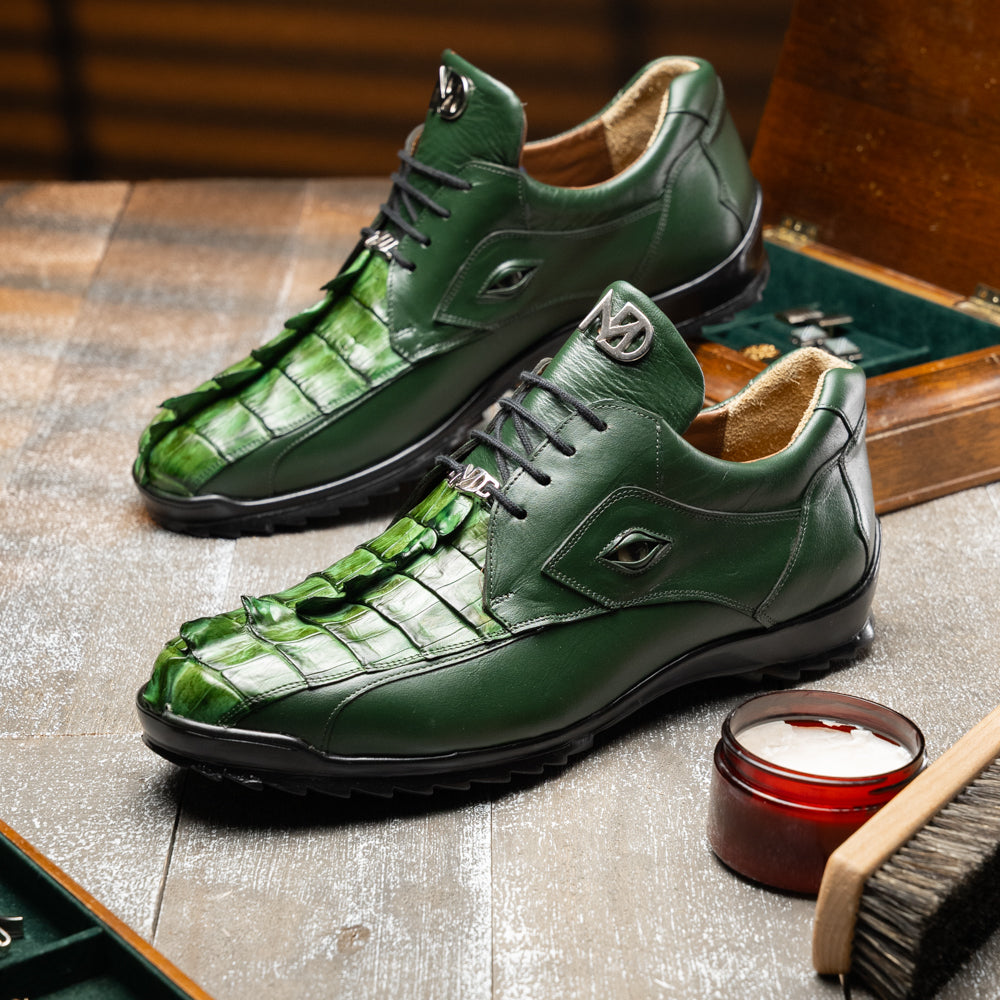 Introducing the Udine Green by Marco Di Milano: luxury men’s shoes in dark green, crafted from exotic hornback caiman leather. These dress shoes showcase a textured, scale-like front design, black laces, and decorative metal initials on the tongue—all displayed against a white background.