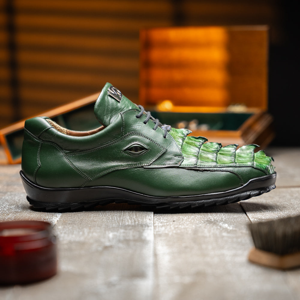 Introducing the Udine Green by Marco Di Milano: luxury men’s shoes in dark green, crafted from exotic hornback caiman leather. These dress shoes showcase a textured, scale-like front design, black laces, and decorative metal initials on the tongue—all displayed against a white background.