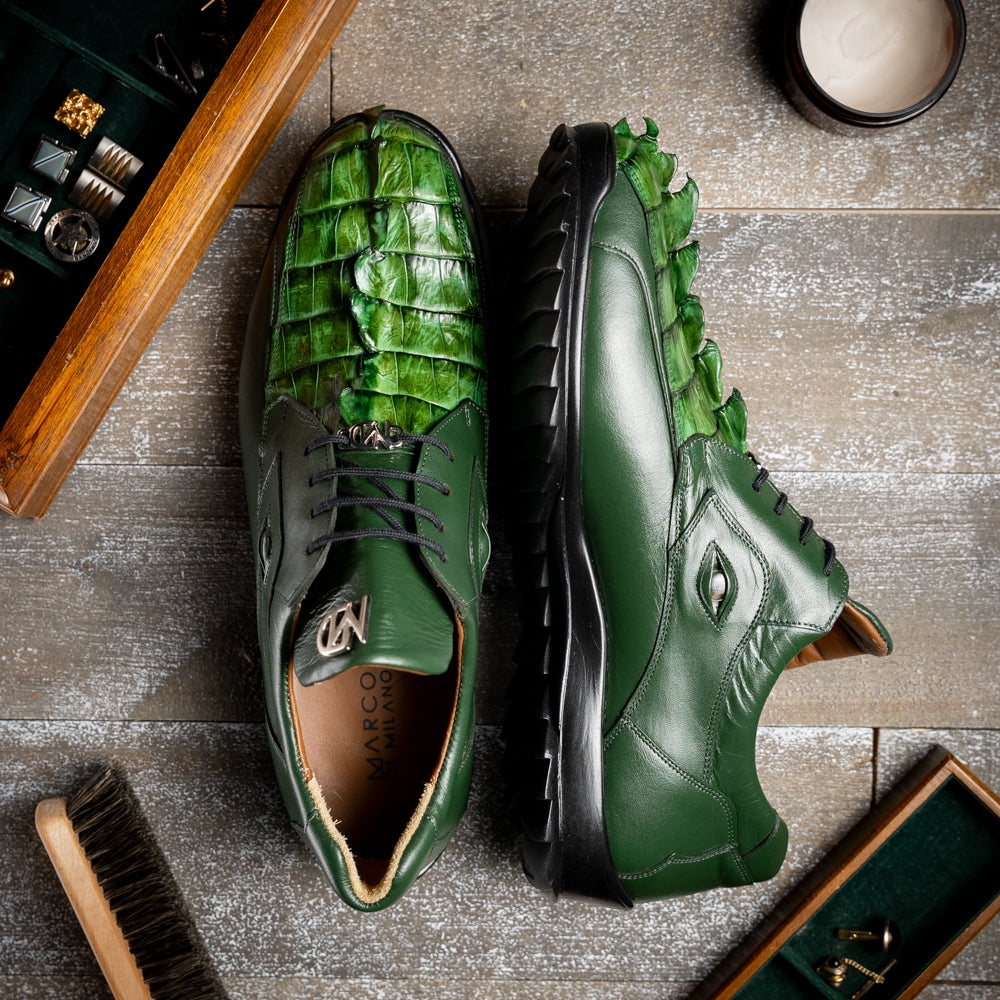 Introducing the Udine Green by Marco Di Milano: luxury men’s shoes in dark green, crafted from exotic hornback caiman leather. These dress shoes showcase a textured, scale-like front design, black laces, and decorative metal initials on the tongue—all displayed against a white background.
