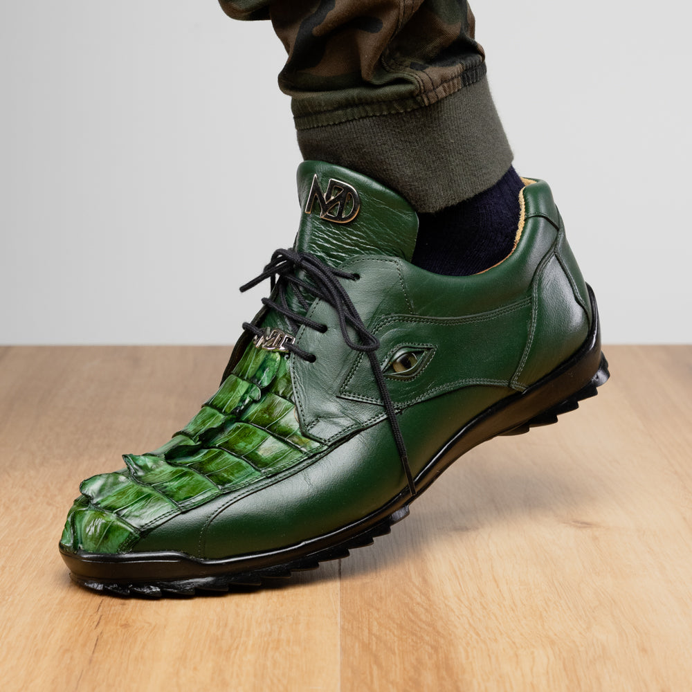 Introducing the Udine Green by Marco Di Milano: luxury men’s shoes in dark green, crafted from exotic hornback caiman leather. These dress shoes showcase a textured, scale-like front design, black laces, and decorative metal initials on the tongue—all displayed against a white background.