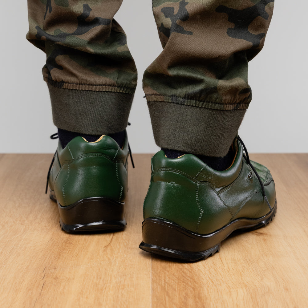 Introducing the Udine Green by Marco Di Milano: luxury men’s shoes in dark green, crafted from exotic hornback caiman leather. These dress shoes showcase a textured, scale-like front design, black laces, and decorative metal initials on the tongue—all displayed against a white background.