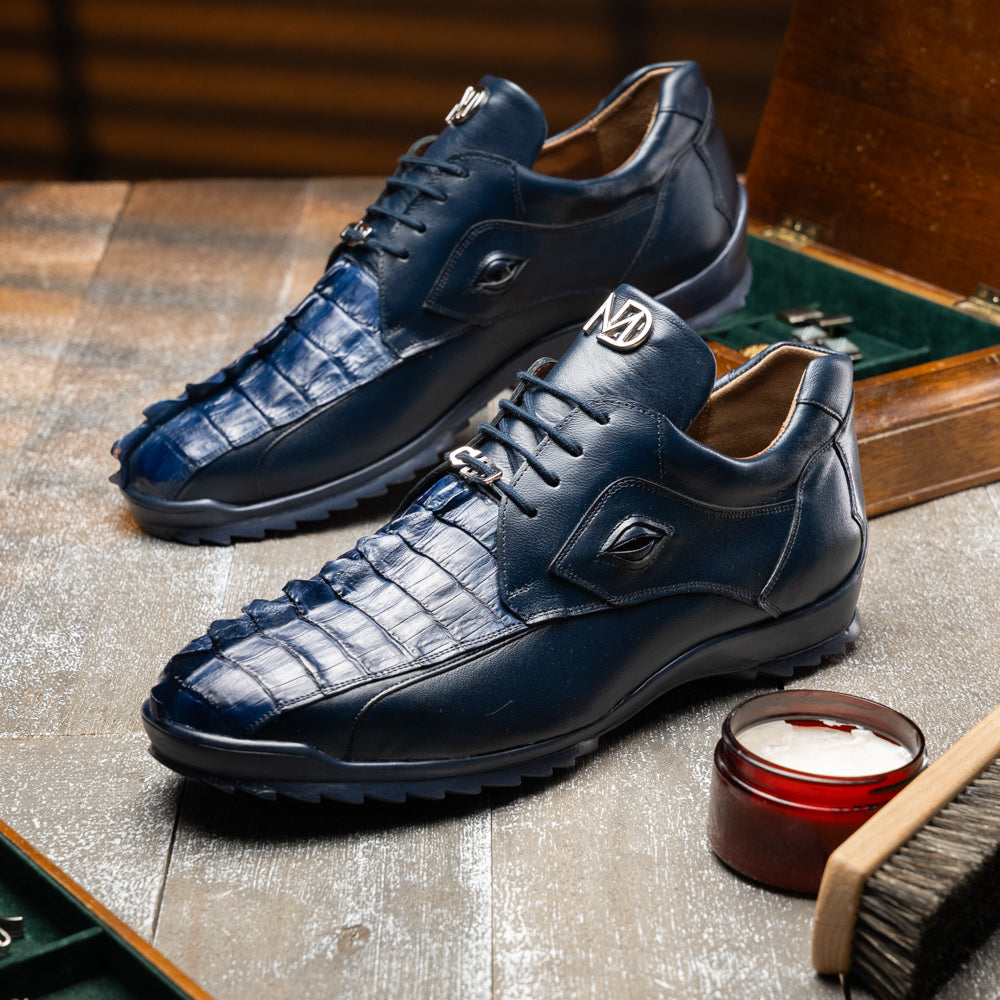 Introducing the Udine Navy by Marco Di Milano—a pair of luxury men’s sneakers crafted from exotic navy blue leather with textured uppers and durable rubber soles. One shoe stands upright while the other rests on its side, showcasing their distinctive style and impeccable craftsmanship.