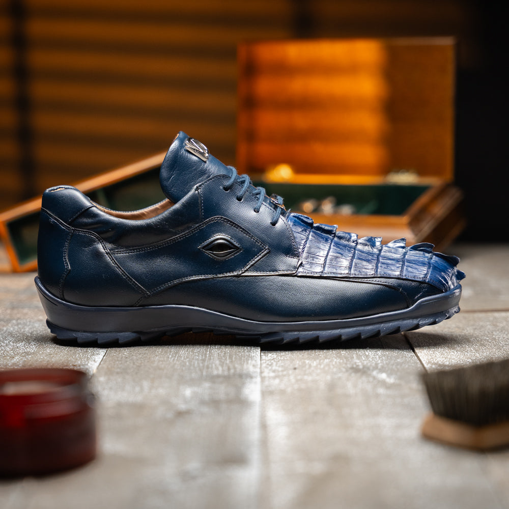 Introducing the Udine Navy by Marco Di Milano—a pair of luxury men’s sneakers crafted from exotic navy blue leather with textured uppers and durable rubber soles. One shoe stands upright while the other rests on its side, showcasing their distinctive style and impeccable craftsmanship.