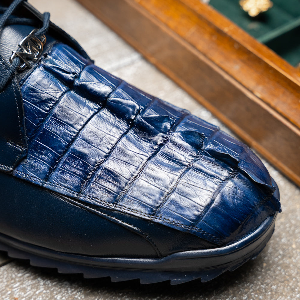Introducing the Udine Navy by Marco Di Milano—a pair of luxury men’s sneakers crafted from exotic navy blue leather with textured uppers and durable rubber soles. One shoe stands upright while the other rests on its side, showcasing their distinctive style and impeccable craftsmanship.
