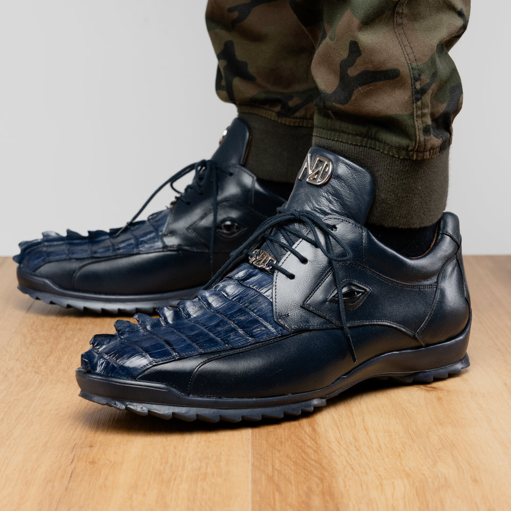 Introducing the Udine Navy by Marco Di Milano—a pair of luxury men’s sneakers crafted from exotic navy blue leather with textured uppers and durable rubber soles. One shoe stands upright while the other rests on its side, showcasing their distinctive style and impeccable craftsmanship.