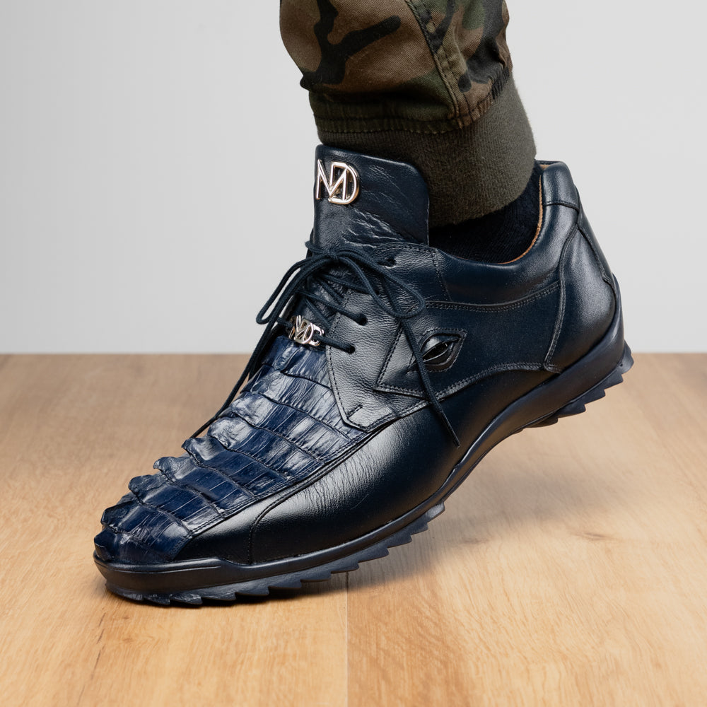 Introducing the Udine Navy by Marco Di Milano—a pair of luxury men’s sneakers crafted from exotic navy blue leather with textured uppers and durable rubber soles. One shoe stands upright while the other rests on its side, showcasing their distinctive style and impeccable craftsmanship.