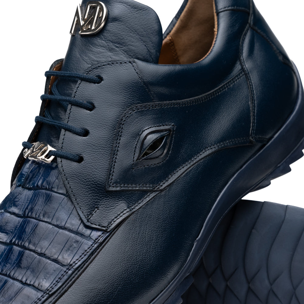Introducing the Udine Navy by Marco Di Milano—a pair of luxury men’s sneakers crafted from exotic navy blue leather with textured uppers and durable rubber soles. One shoe stands upright while the other rests on its side, showcasing their distinctive style and impeccable craftsmanship.
