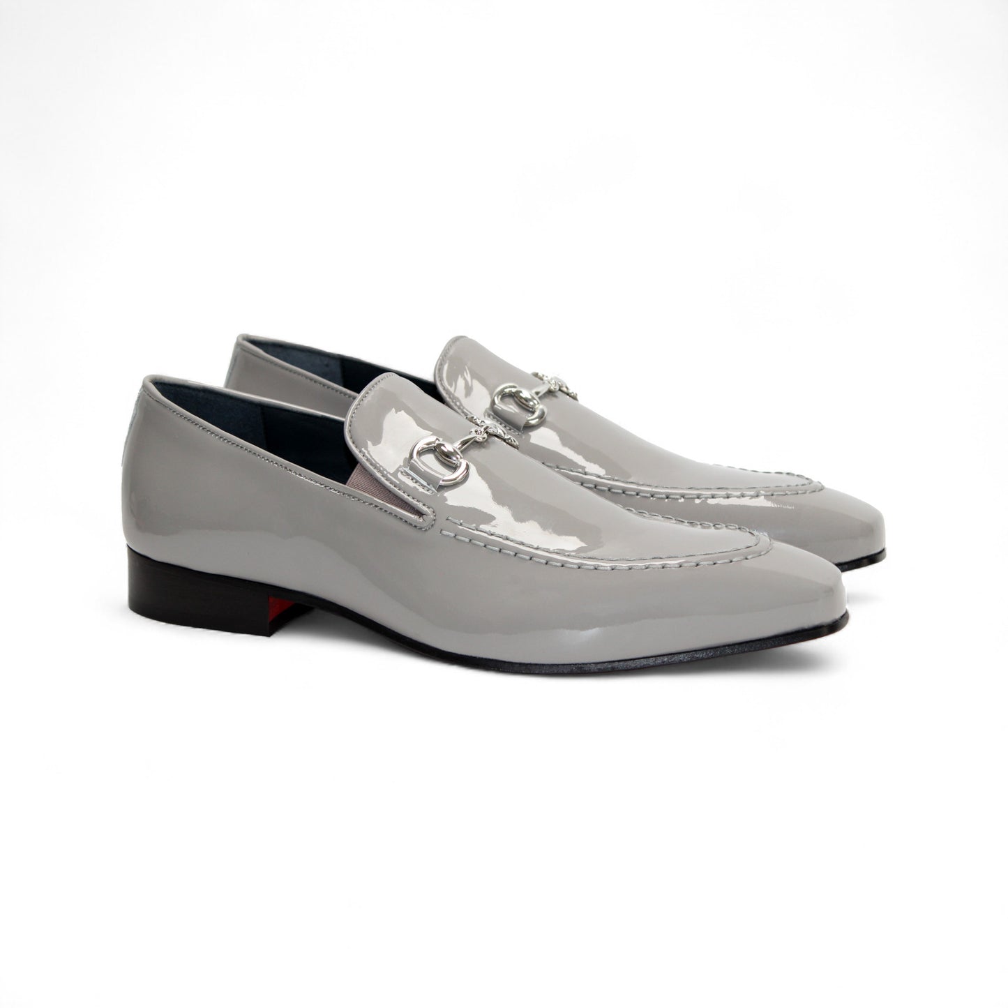 The Duca Di Matiste Duca Valenza Grey loafer features a glossy light gray finish, metal bit detail, black sole, and low heel—exemplifying Italian craftsmanship in luxury footwear. Shown in side profile on a white background.
