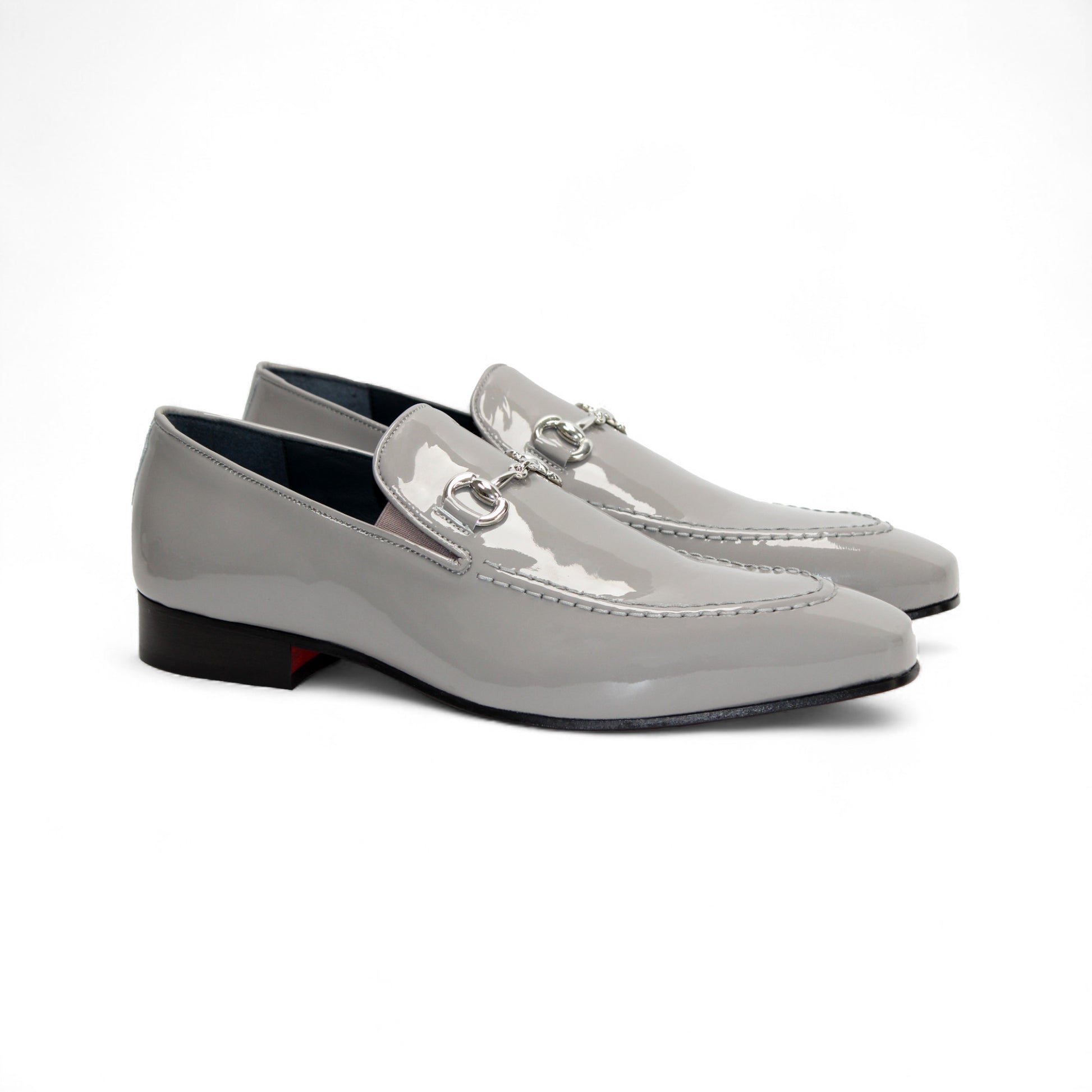 The Duca Di Matiste Duca Valenza Grey loafer features a glossy light gray finish, metal bit detail, black sole, and low heel—exemplifying Italian craftsmanship in luxury footwear. Shown in side profile on a white background.