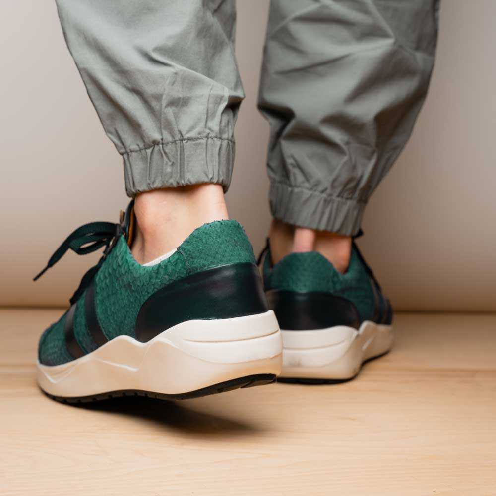 The Marco Di Milano Verona Green sneakers are luxury shoes with scale-like patterns, dark green accents, and white soles. One shoe is upright while the other lies on its side.