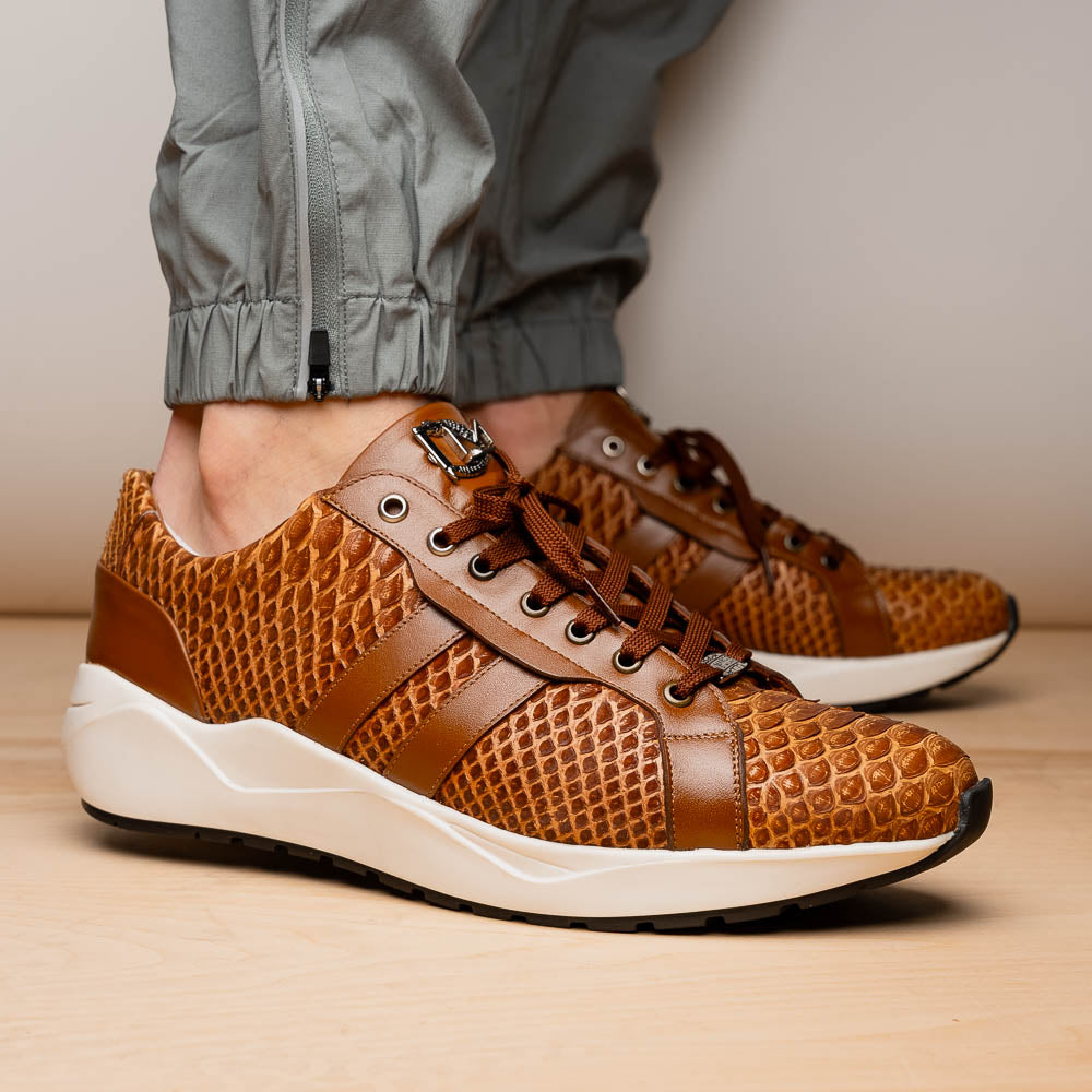 The Marco Di Milano Verona Honey is a brown luxury sneaker with a textured, reptile-like pattern, leather accents, brown laces, and a white sole. One men’s genuine calfskin shoe stands upright; the other displays its sole.