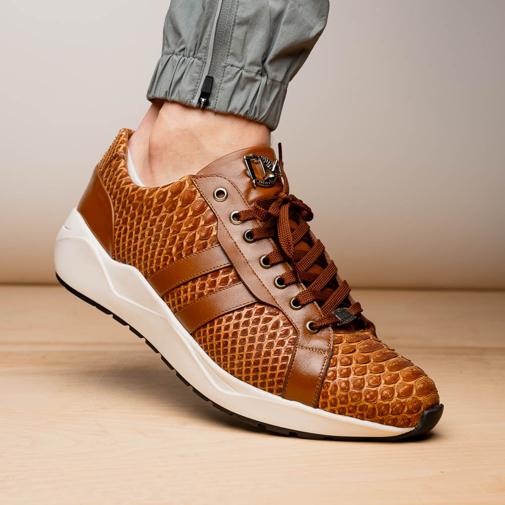 The Marco Di Milano Verona Honey is a brown luxury sneaker with a textured, reptile-like pattern, leather accents, brown laces, and a white sole. One men’s genuine calfskin shoe stands upright; the other displays its sole.