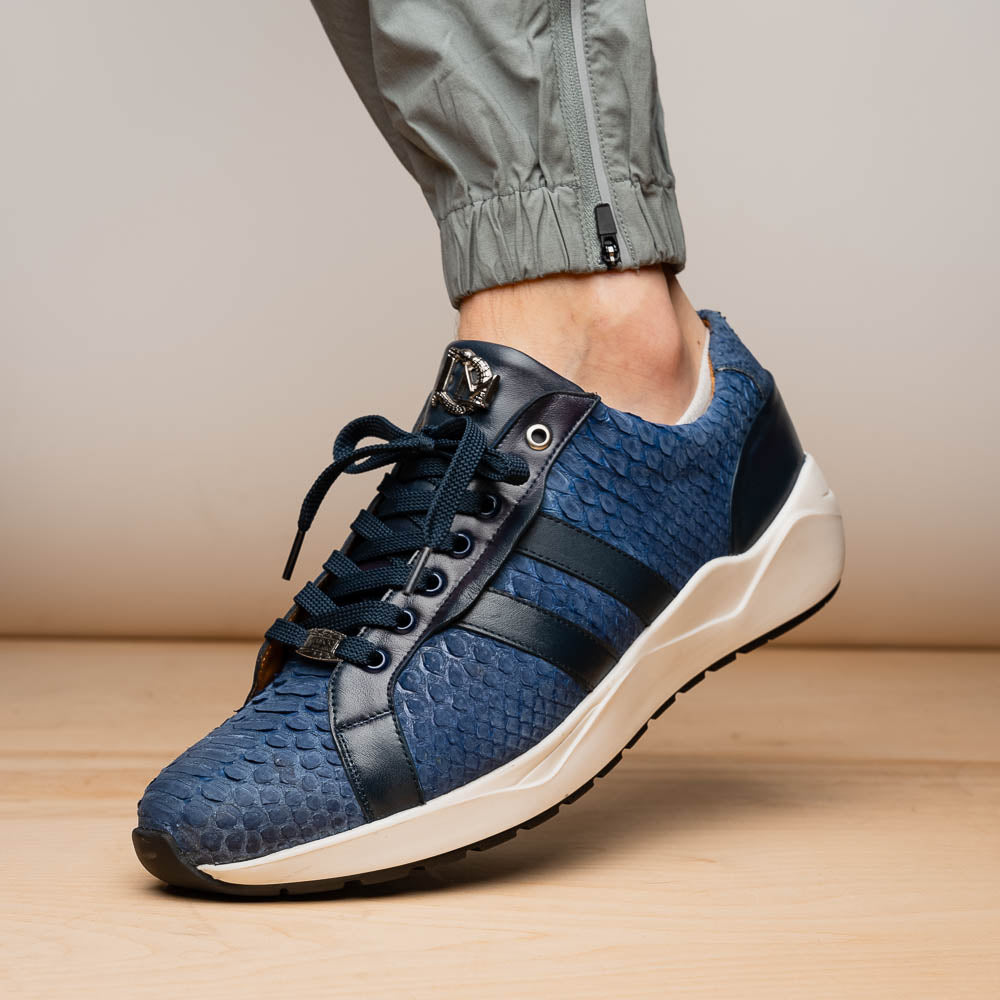 The Verona Navy sneakers by Marco Di Milano feature a blue python texture, navy laces, side stripes, and white rubber soles—luxury footwear with one shoe upright and the other on its side.