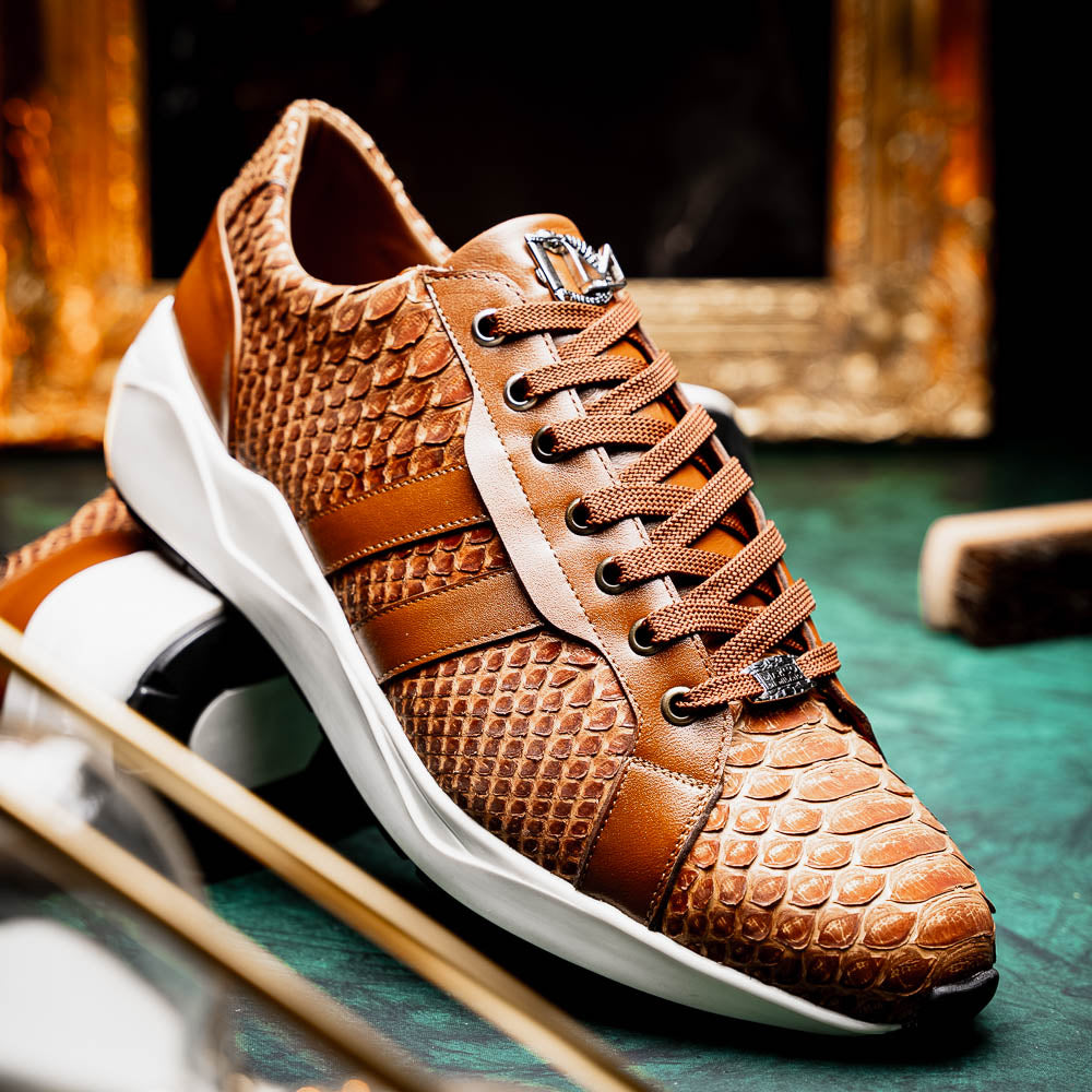 The Marco Di Milano Verona Honey is a brown luxury sneaker with a textured, reptile-like pattern, leather accents, brown laces, and a white sole. One men’s genuine calfskin shoe stands upright; the other displays its sole.