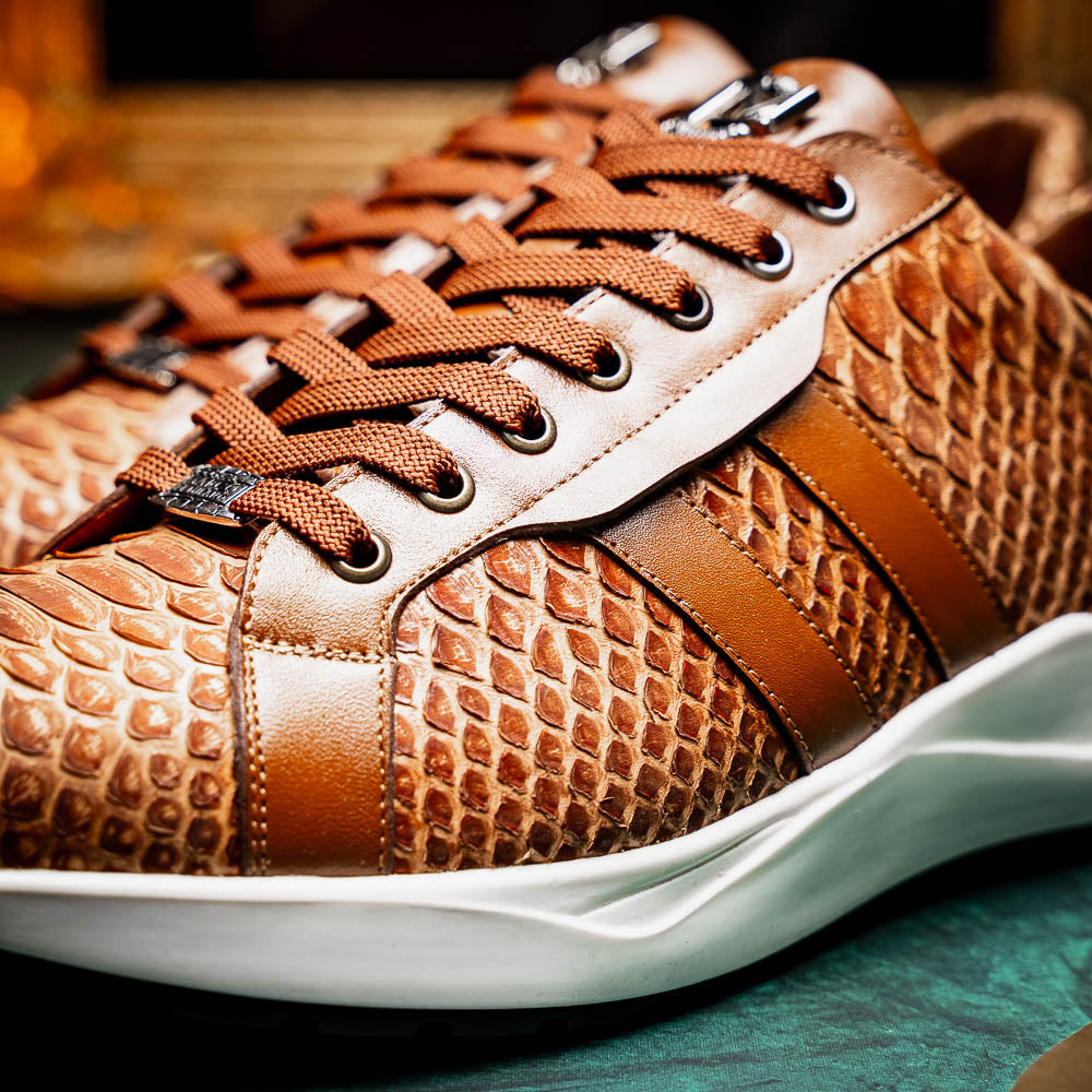 The Marco Di Milano Verona Honey is a brown luxury sneaker with a textured, reptile-like pattern, leather accents, brown laces, and a white sole. One men’s genuine calfskin shoe stands upright; the other displays its sole.