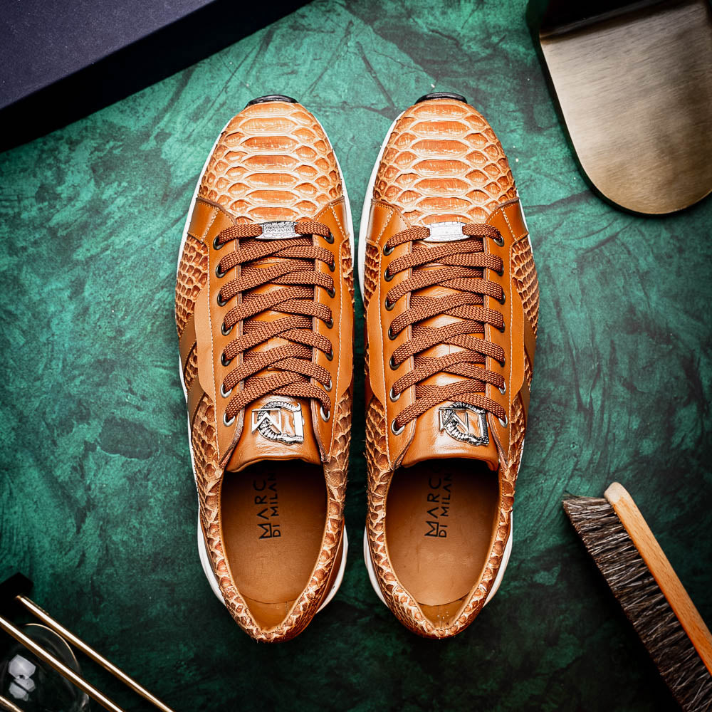 The Marco Di Milano Verona Honey is a brown luxury sneaker with a textured, reptile-like pattern, leather accents, brown laces, and a white sole. One men’s genuine calfskin shoe stands upright; the other displays its sole.