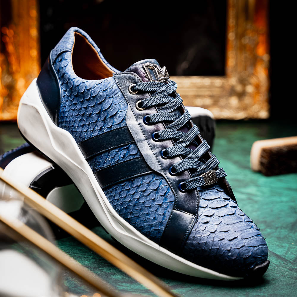 The Verona Navy sneakers by Marco Di Milano feature a blue python texture, navy laces, side stripes, and white rubber soles—luxury footwear with one shoe upright and the other on its side.