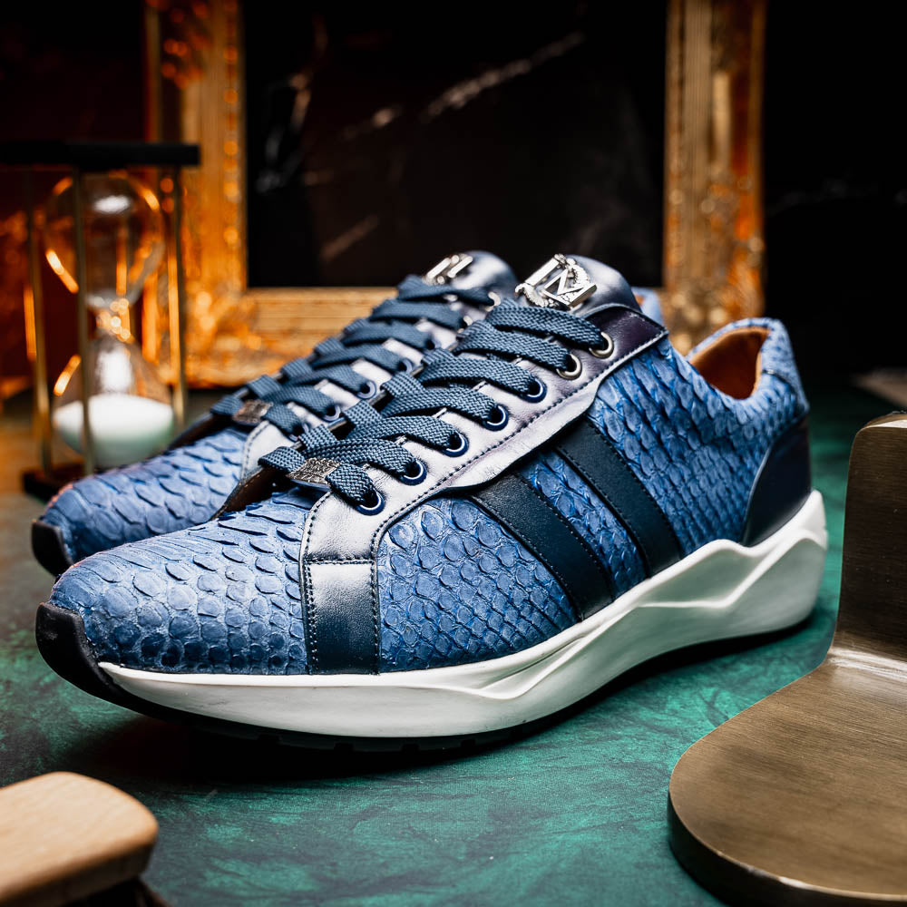 The Verona Navy sneakers by Marco Di Milano feature a blue python texture, navy laces, side stripes, and white rubber soles—luxury footwear with one shoe upright and the other on its side.