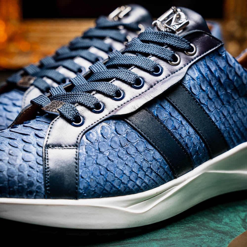 The Verona Navy sneakers by Marco Di Milano feature a blue python texture, navy laces, side stripes, and white rubber soles—luxury footwear with one shoe upright and the other on its side.