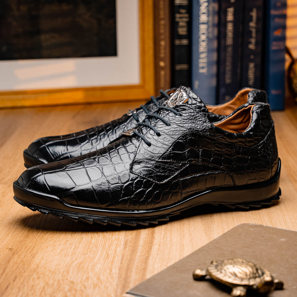 The Vulcan Black by Marco Di Milano are black, crocodile-patterned leather dress shoes with rubber soles—one upright and one displaying the sole. This luxury footwear features hand-painted finishes for a truly refined look.