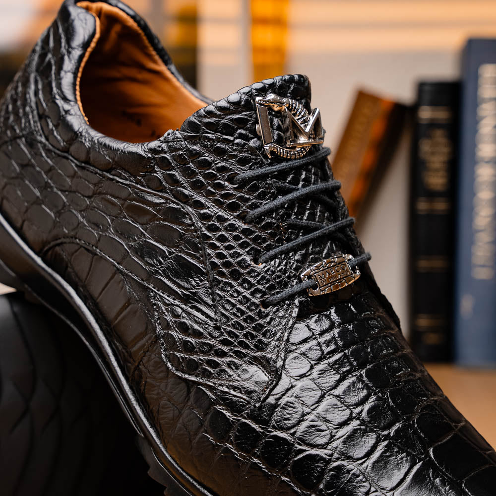 The Vulcan Black by Marco Di Milano are black, crocodile-patterned leather dress shoes with rubber soles—one upright and one displaying the sole. This luxury footwear features hand-painted finishes for a truly refined look.