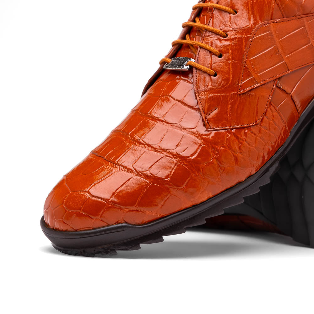 The Marco Di Milano Vulcan Honey features orange, crocodile-patterned leather dress shoes with hand-painted finishes and black rubber soles; one shoe stands upright while the other rests on its side below.