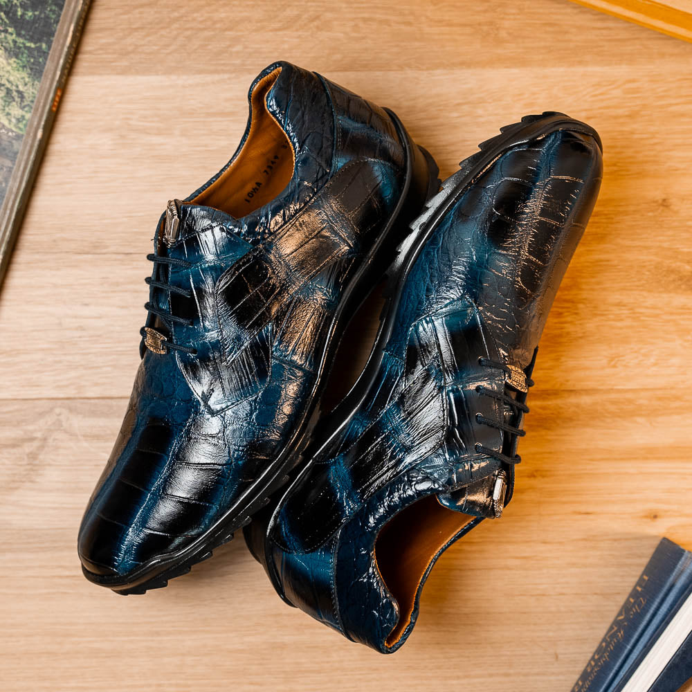 The Vulcan Rustic Navy by Marco Di Milano features glossy blue and black lace-up dress shoes with textured leather, rubber soles, and exquisite hand-painted finishes—one upright, the other propped beneath it—showcasing luxury footwear.