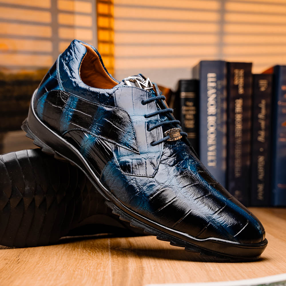 The Vulcan Rustic Navy by Marco Di Milano features glossy blue and black lace-up dress shoes with textured leather, rubber soles, and exquisite hand-painted finishes—one upright, the other propped beneath it—showcasing luxury footwear.