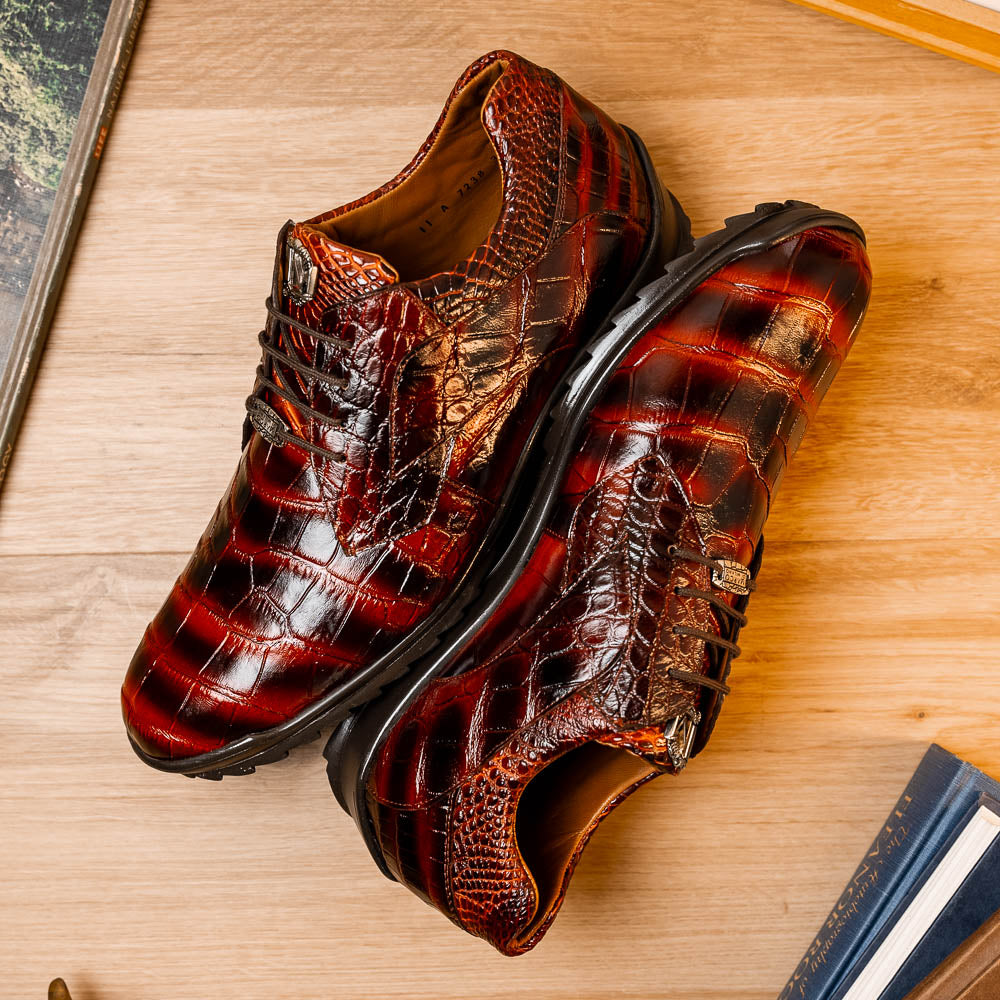 The Vulcan Rustic Cognac by Marco Di Milano features brown crocodile-pattern leather dress shoes with black rubber soles, one shoe upright and the other tilted—showcasing luxury footwear with exquisite hand-painted finishes.