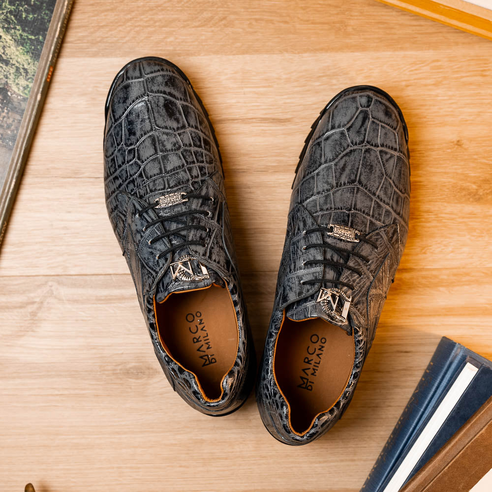 A pair of Marco Di Milano Vulcan Rustic Gray men's dress shoes, showcasing luxury footwear with crocodile-patterned leather, hand-painted finishes, and metal lace accents—one upright, one on its side to display the sole.
