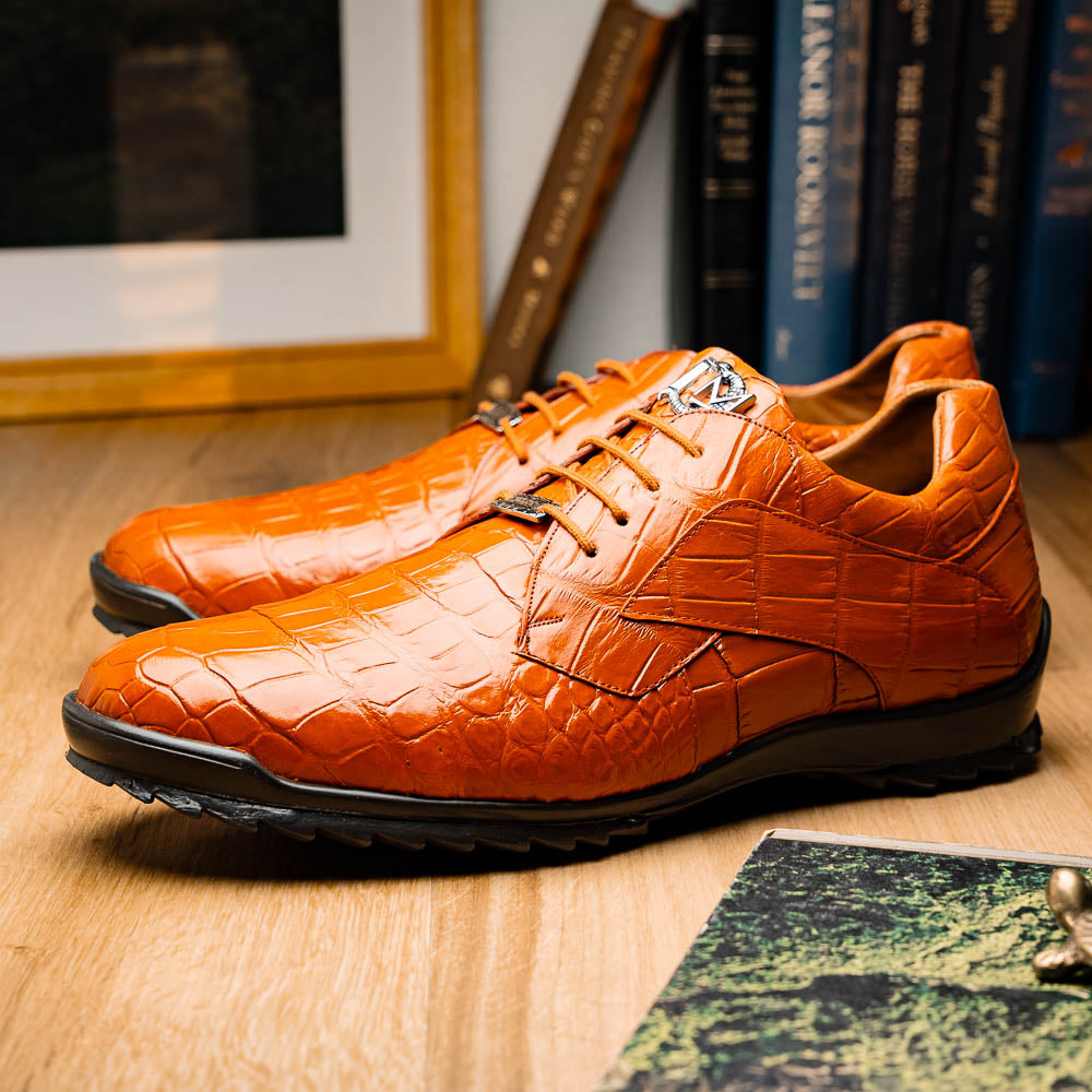 The Marco Di Milano Vulcan Honey features orange, crocodile-patterned leather dress shoes with hand-painted finishes and black rubber soles; one shoe stands upright while the other rests on its side below.