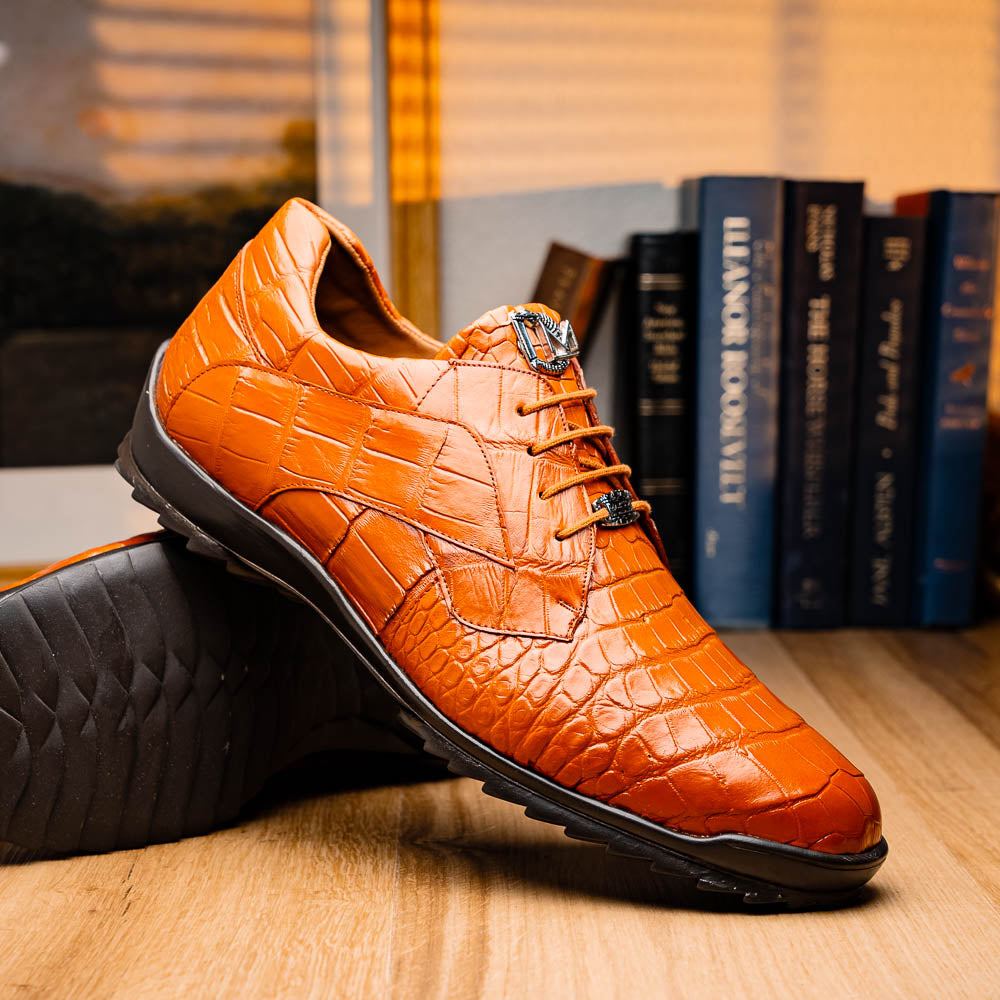 The Marco Di Milano Vulcan Honey features orange, crocodile-patterned leather dress shoes with hand-painted finishes and black rubber soles; one shoe stands upright while the other rests on its side below.