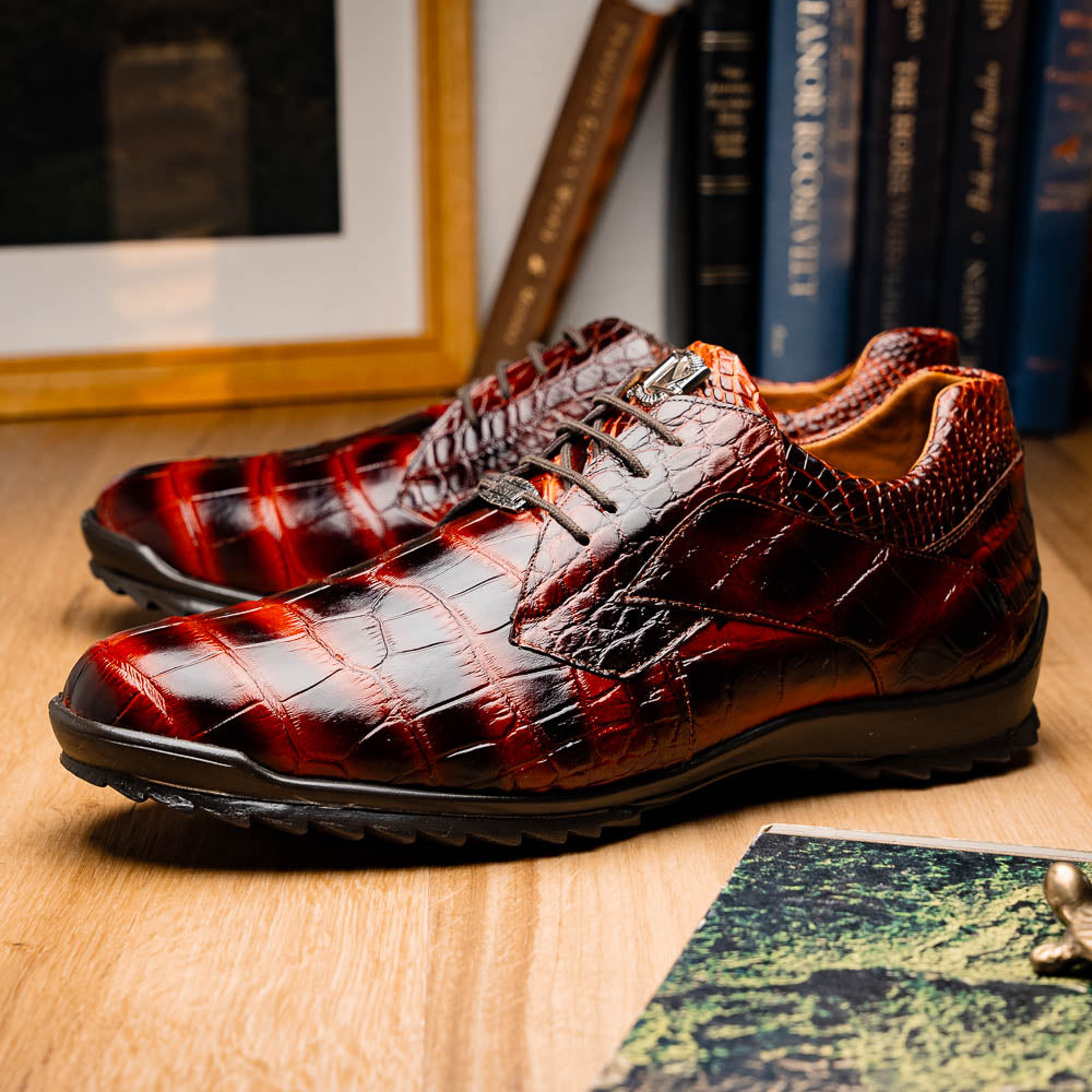 The Vulcan Rustic Cognac by Marco Di Milano features brown crocodile-pattern leather dress shoes with black rubber soles, one shoe upright and the other tilted—showcasing luxury footwear with exquisite hand-painted finishes.