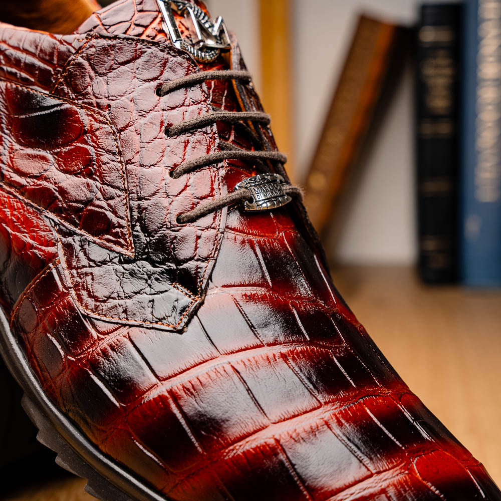 The Vulcan Rustic Cognac by Marco Di Milano features brown crocodile-pattern leather dress shoes with black rubber soles, one shoe upright and the other tilted—showcasing luxury footwear with exquisite hand-painted finishes.