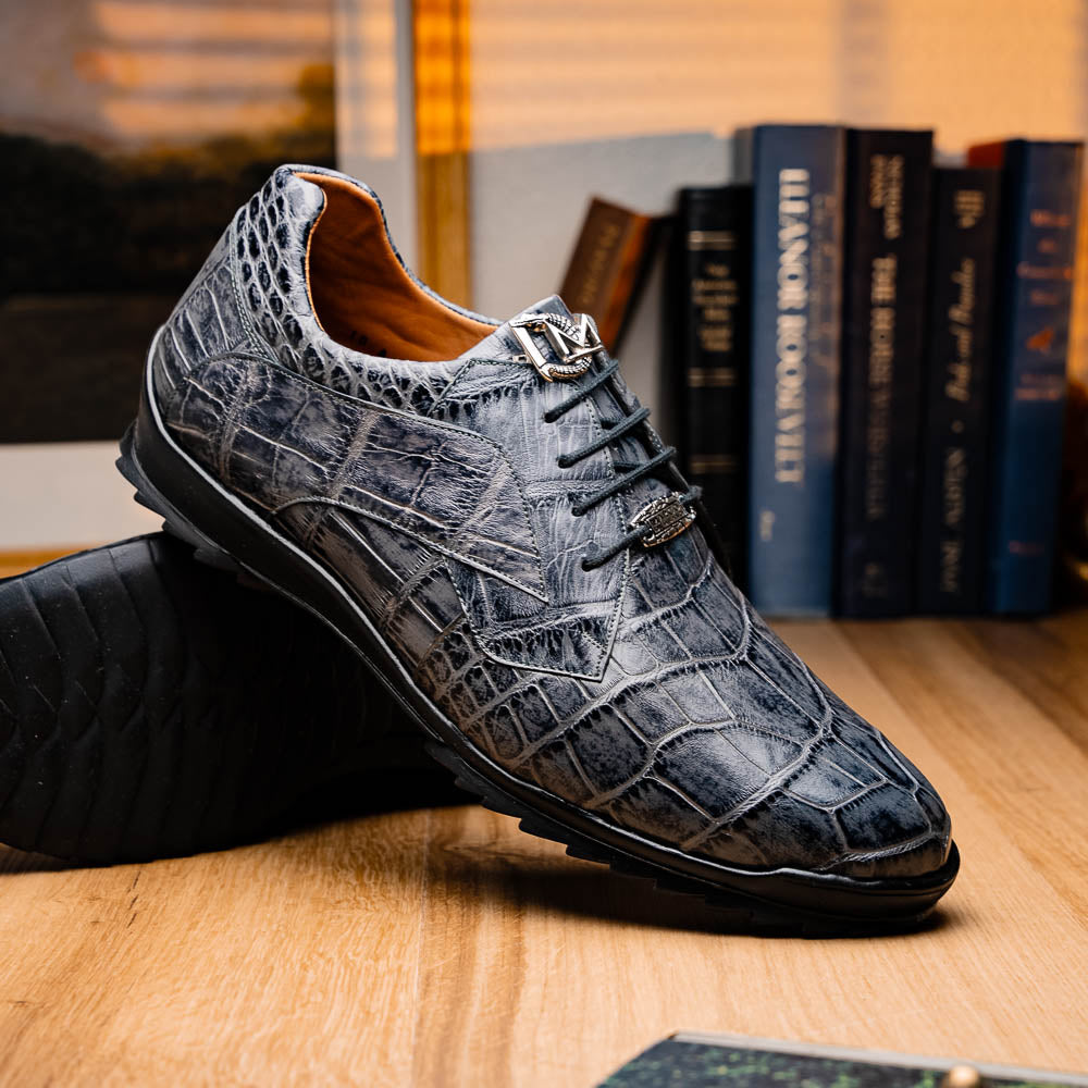 A pair of Marco Di Milano Vulcan Rustic Gray men's dress shoes, showcasing luxury footwear with crocodile-patterned leather, hand-painted finishes, and metal lace accents—one upright, one on its side to display the sole.