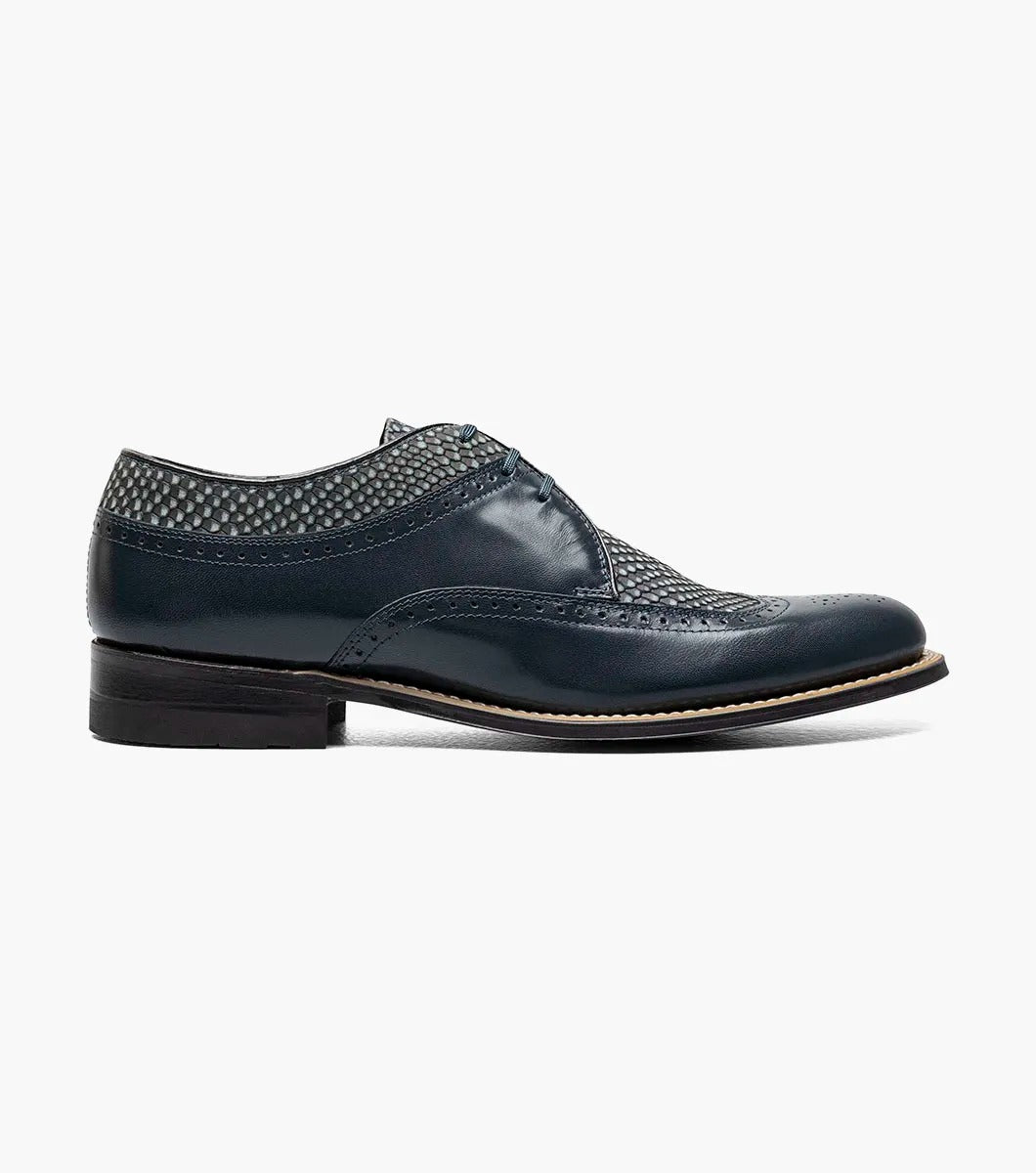 The Stacy Adams DAYTON Python Print Wingtip Oxford in navy is a sophisticated shoe, showcasing textured paneling and made from Kidskin leather. It includes sleek black laces and a polished wooden sole.